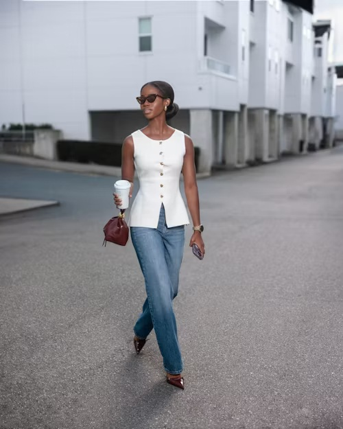 femeie de culoare în jeans și bluză albă cu cafea în mână