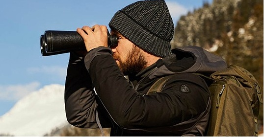 bărbat cu căciulă și geacă se uită prin binoclu